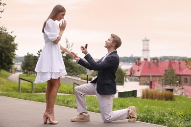 Photo of Smiling man with engagement ring making marriage proposal to his surprised girlfriend outdoors