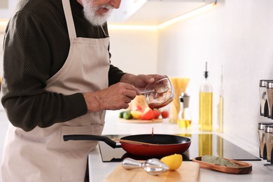 Photo of Elderly man cooking dish on cooktop in kitchen, closeup