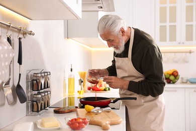 Photo of Elderly man cooking dish on cooktop in kitchen