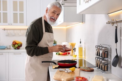 Photo of Elderly man cooking dish on cooktop in kitchen