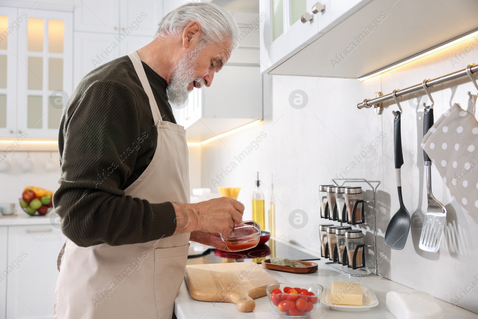 Elderly man cooking at countertop in kitchen Photo of Elderly man cooking at countertop in kitchen