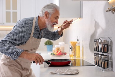 Photo of Elderly man cooking dish on cooktop in kitchen