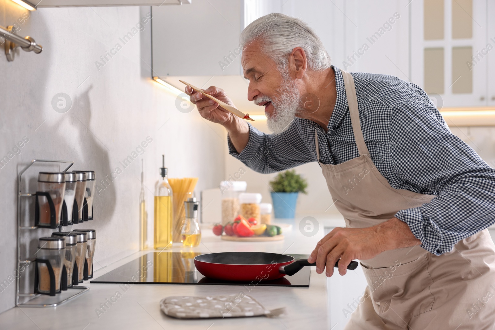 Elderly man cooking dish on cooktop in kitchen Photo of Elderly man cooking dish on cooktop in kitchen
