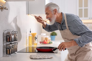 Photo of Elderly man cooking dish on cooktop in kitchen