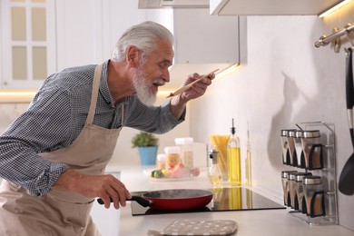 Photo of Elderly man cooking dish on cooktop in kitchen