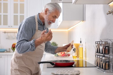 Photo of Elderly man cooking dish on cooktop in kitchen