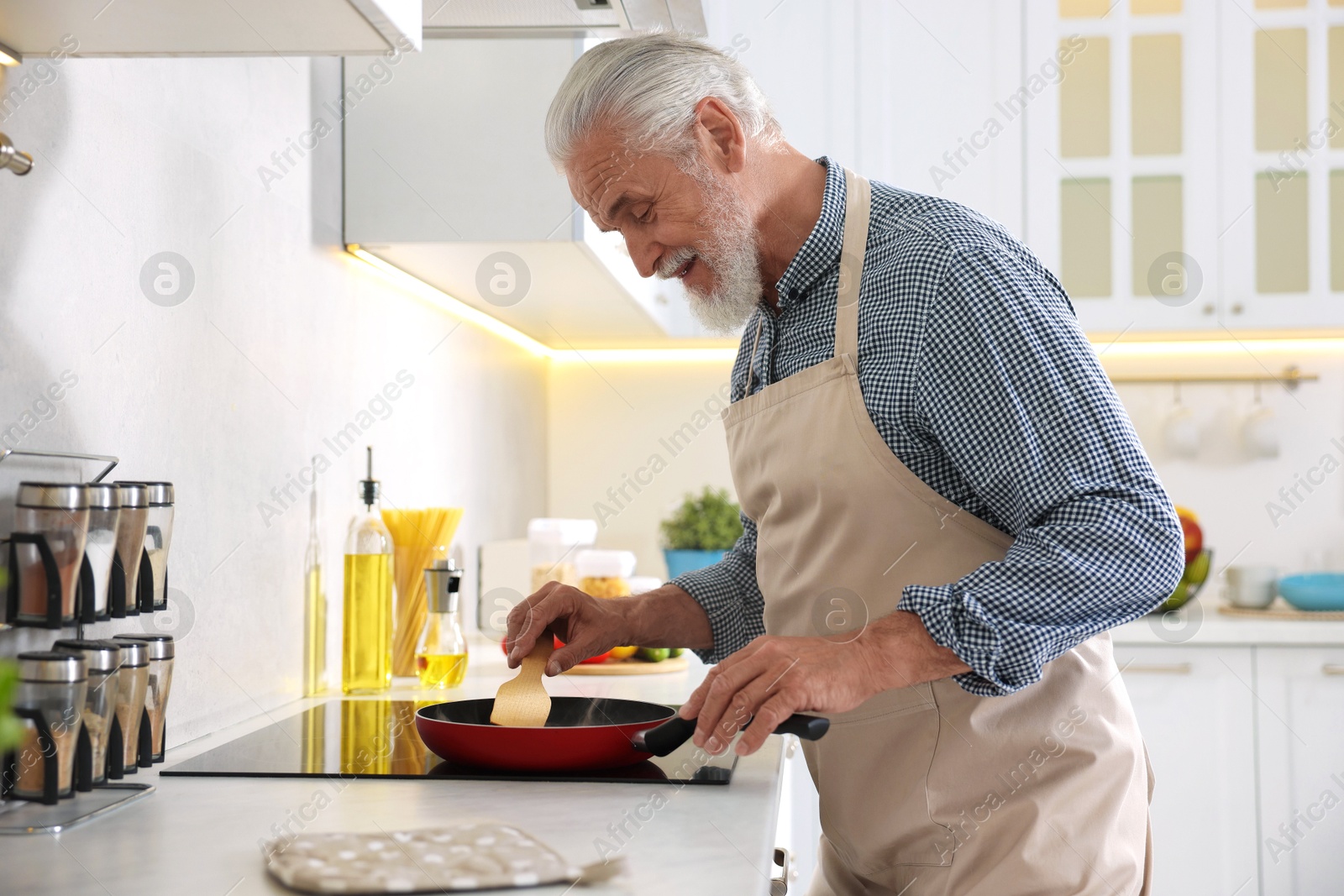 Elderly man cooking dish on cooktop in kitchen Photo of Elderly man cooking dish on cooktop in kitchen