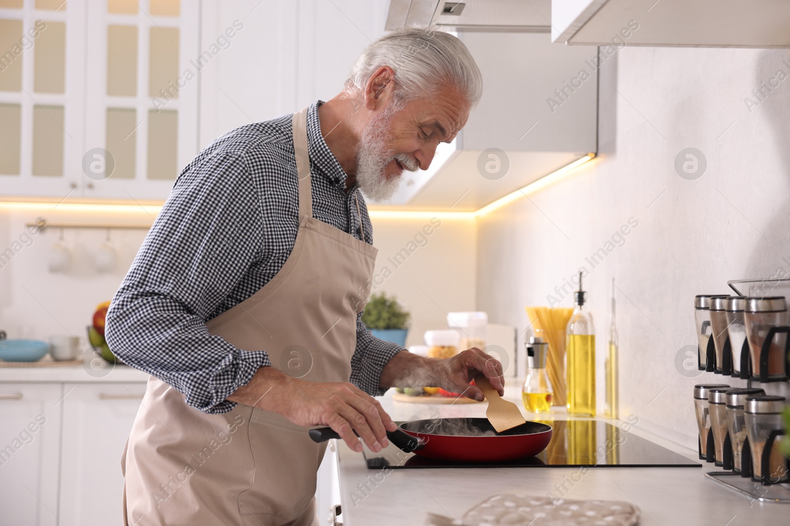 Elderly man cooking dish on cooktop in kitchen Photo of Elderly man cooking dish on cooktop in kitchen