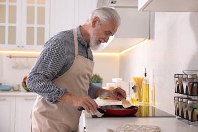Photo of Elderly man cooking dish on cooktop in kitchen