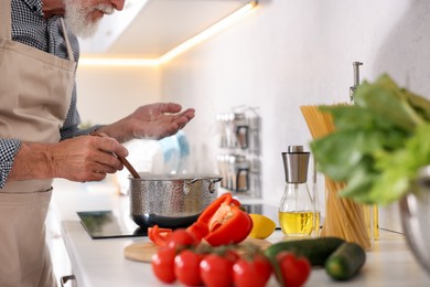 Photo of Elderly man cooking dish on cooktop in kitchen, closeup