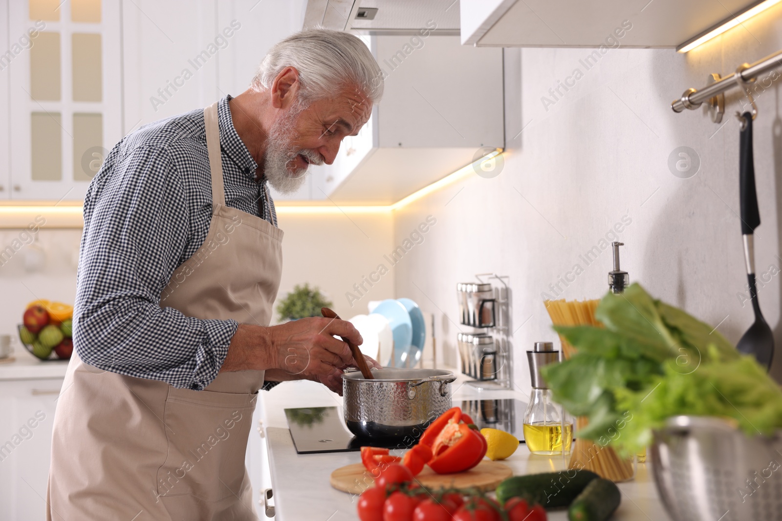 Elderly man cooking dish on cooktop in kitchen Photo of Elderly man cooking dish on cooktop in kitchen