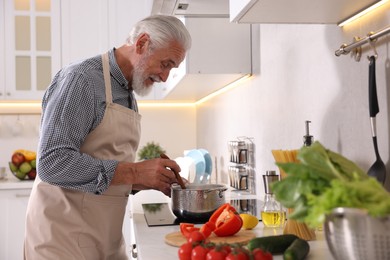 Photo of Elderly man cooking dish on cooktop in kitchen