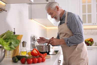 Photo of Elderly man cooking dish on cooktop in kitchen