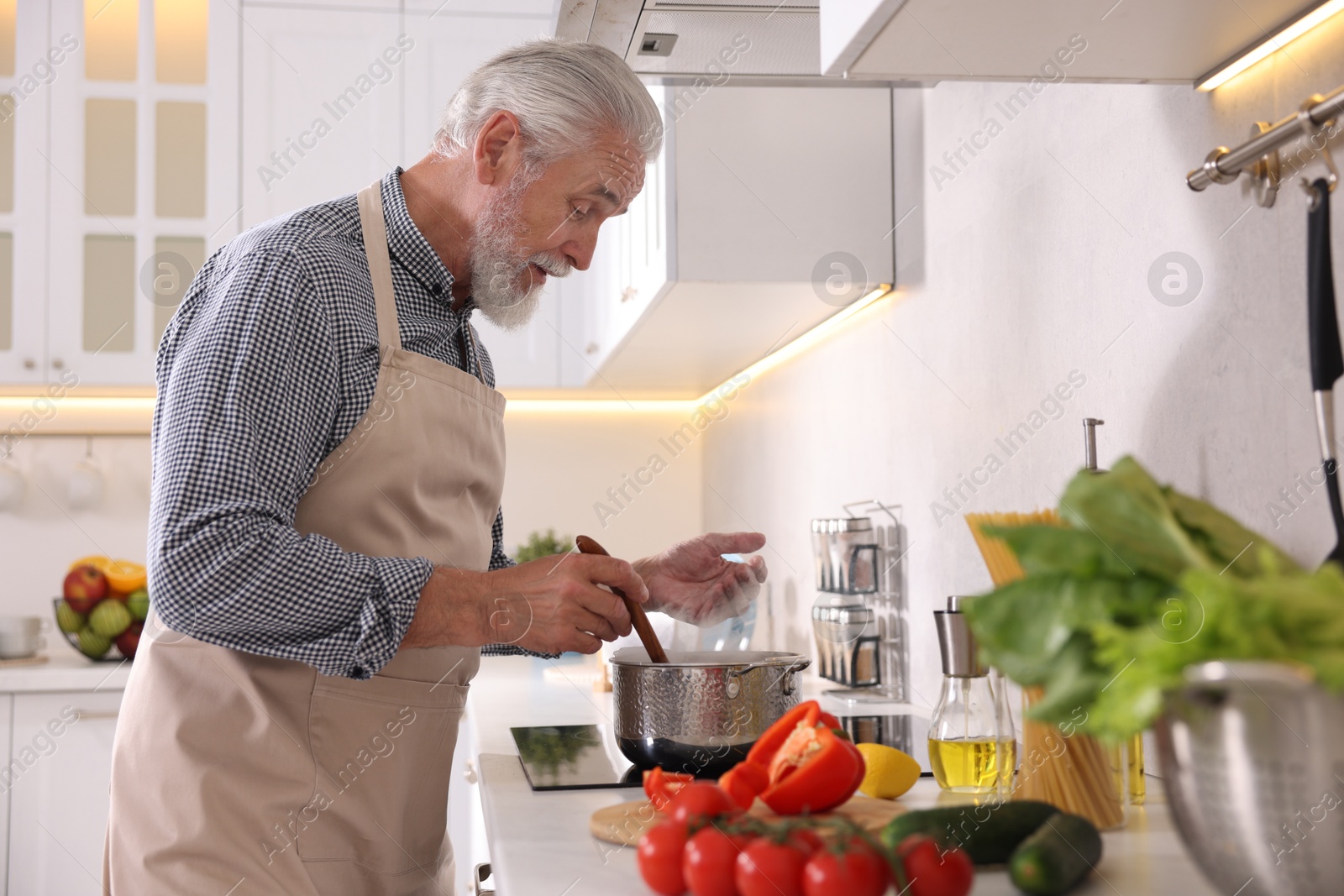 Elderly man cooking dish on cooktop in kitchen Photo of Elderly man cooking dish on cooktop in kitchen