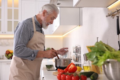 Photo of Elderly man cooking dish on cooktop in kitchen