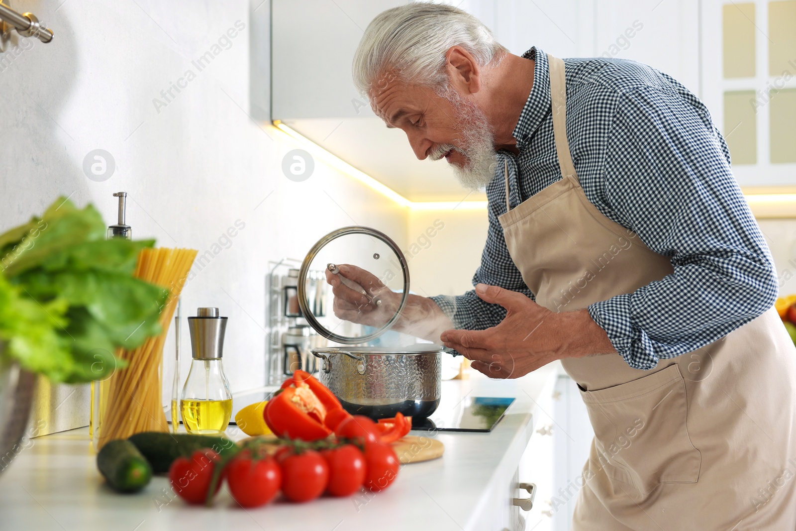 Elderly man cooking dish on cooktop in kitchen Photo of Elderly man cooking dish on cooktop in kitchen