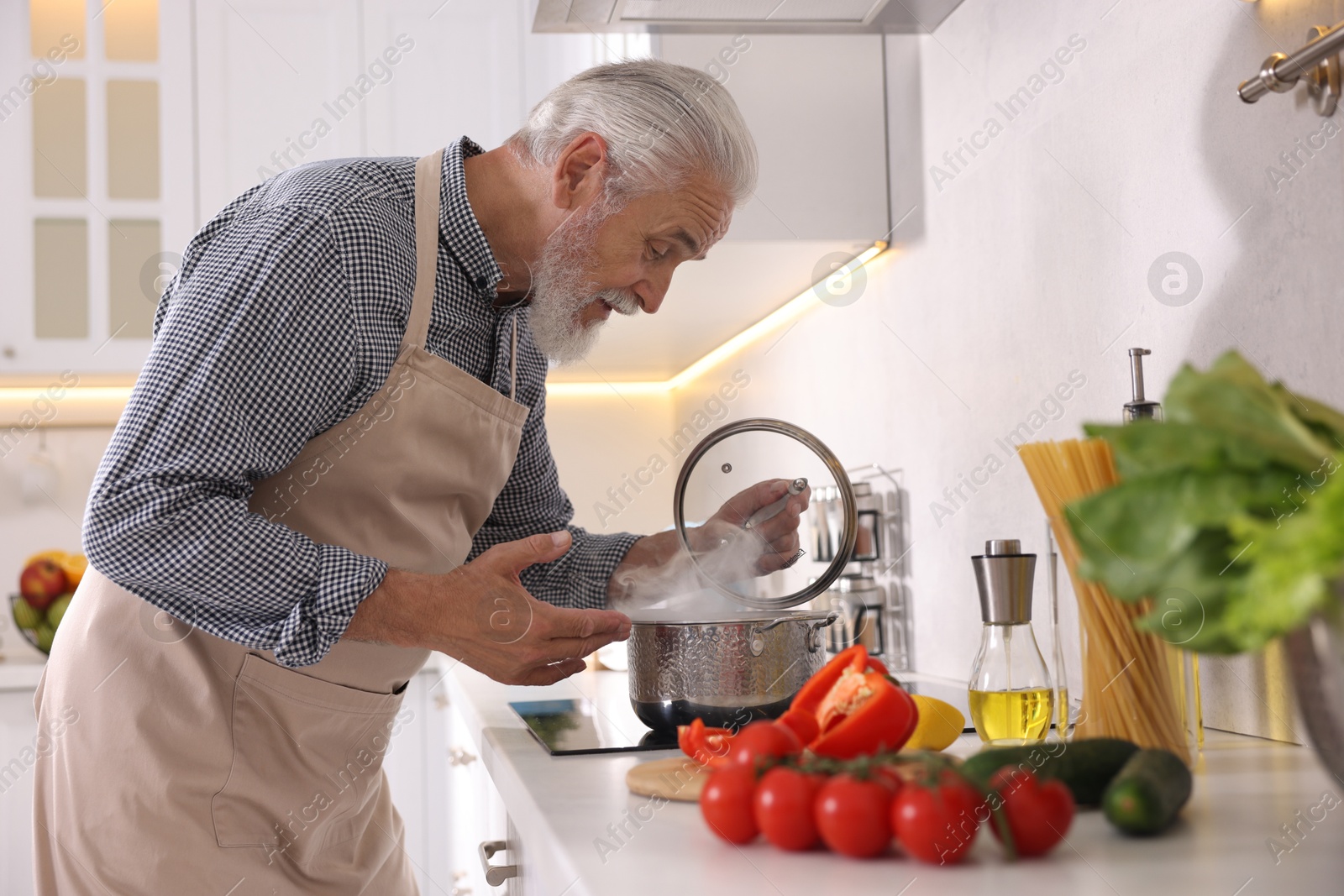 Elderly man cooking dish on cooktop in kitchen Photo of Elderly man cooking dish on cooktop in kitchen