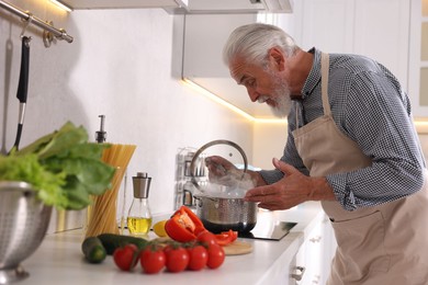 Photo of Elderly man cooking dish on cooktop in kitchen