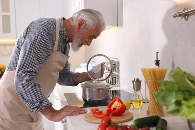 Photo of Elderly man cooking dish on cooktop in kitchen