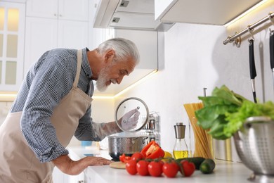 Photo of Elderly man cooking dish on cooktop in kitchen