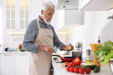 Photo of Elderly man cooking dish on cooktop in kitchen