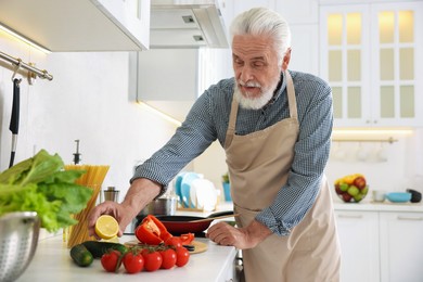Photo of Elderly man cooking dish on cooktop in kitchen