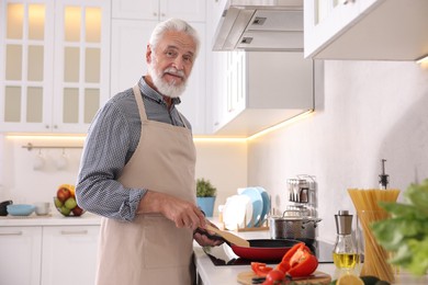 Photo of Elderly man cooking dish on cooktop in kitchen