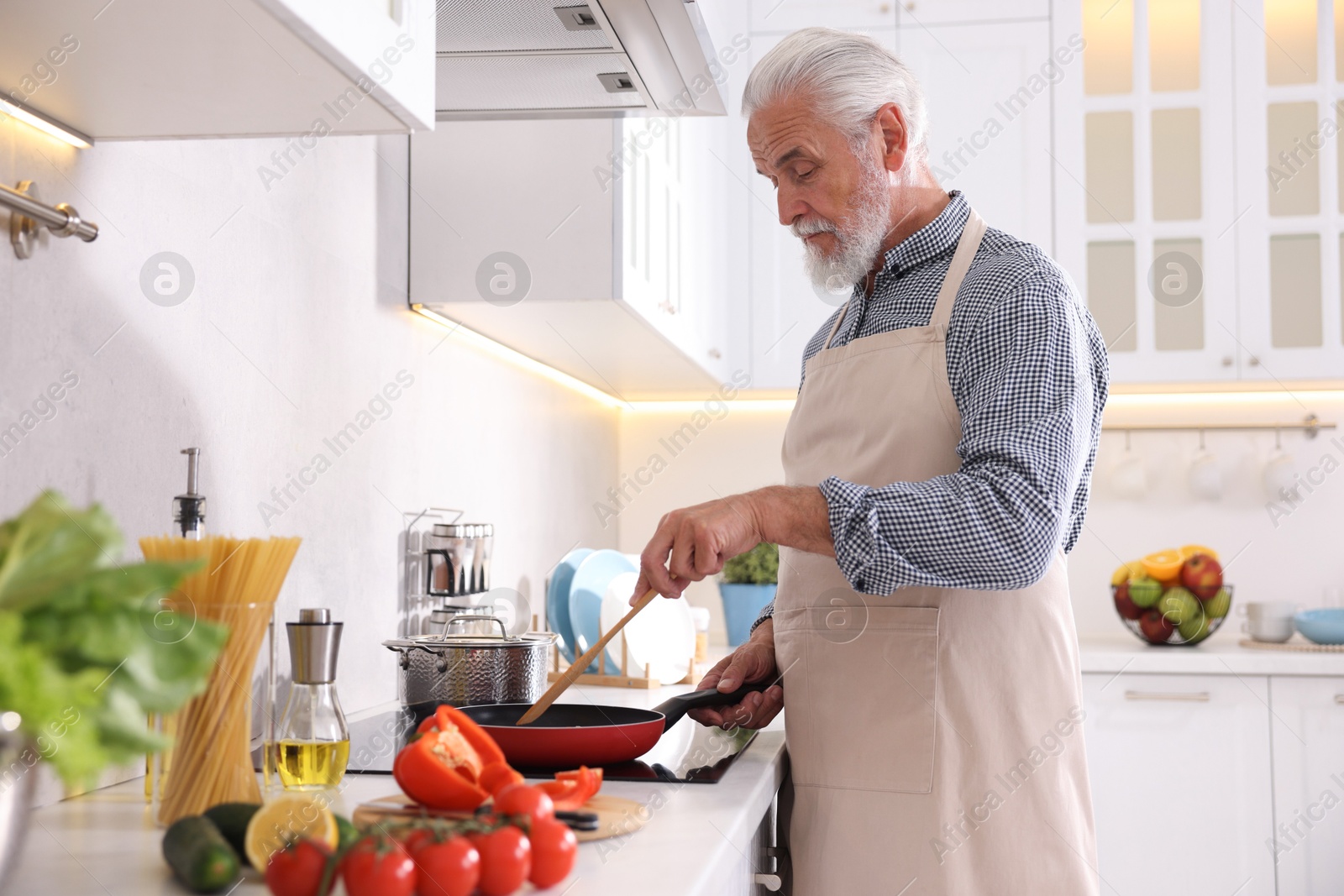 Elderly man cooking dish on cooktop in kitchen Photo of Elderly man cooking dish on cooktop in kitchen
