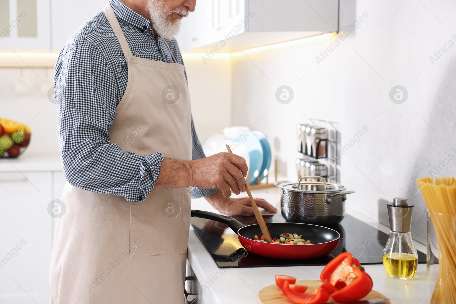 Elderly man cooking dish on cooktop in kitchen, closeup Photo of Elderly man cooking dish on cooktop in kitchen, closeup