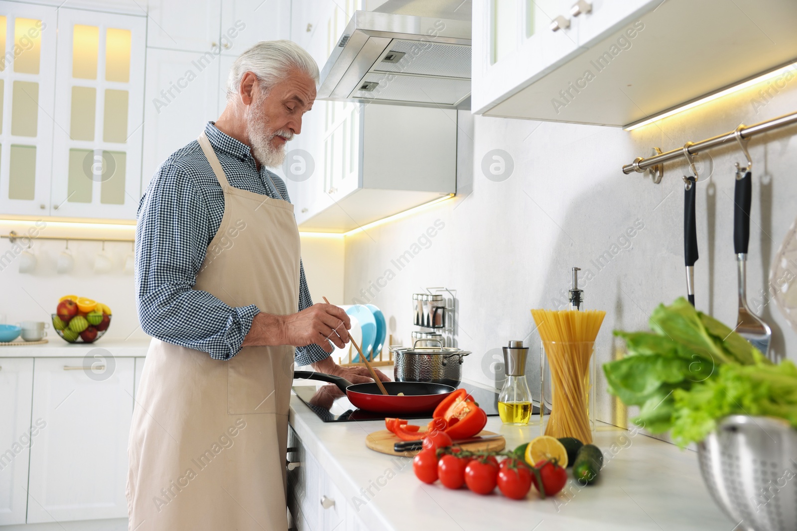 Elderly man cooking dish on cooktop in kitchen Photo of Elderly man cooking dish on cooktop in kitchen