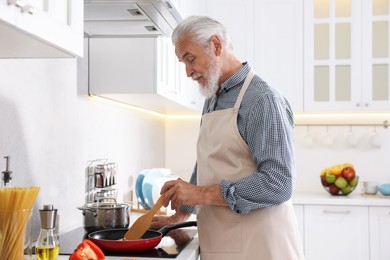Photo of Elderly man cooking dish on cooktop in kitchen