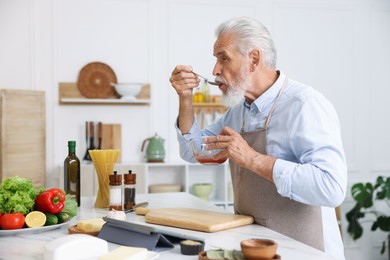 Photo of Elderly man cooking at white marble table in kitchen