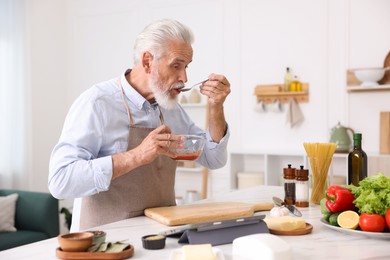 Photo of Elderly man cooking at white marble table in kitchen