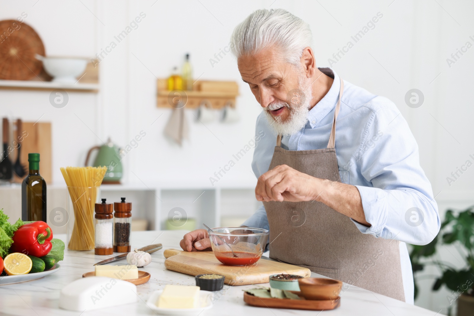 Elderly man cooking at white marble table in kitchen Photo of Elderly man cooking at white marble table in kitchen