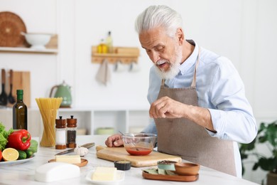 Photo of Elderly man cooking at white marble table in kitchen