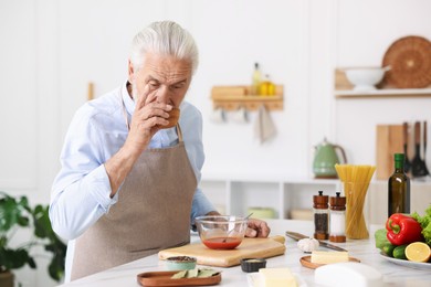 Photo of Elderly man cooking at white marble table in kitchen