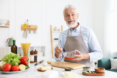 Photo of Elderly man cooking at white marble table in kitchen