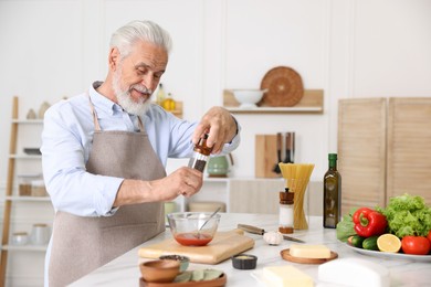 Photo of Elderly man cooking at white marble table in kitchen