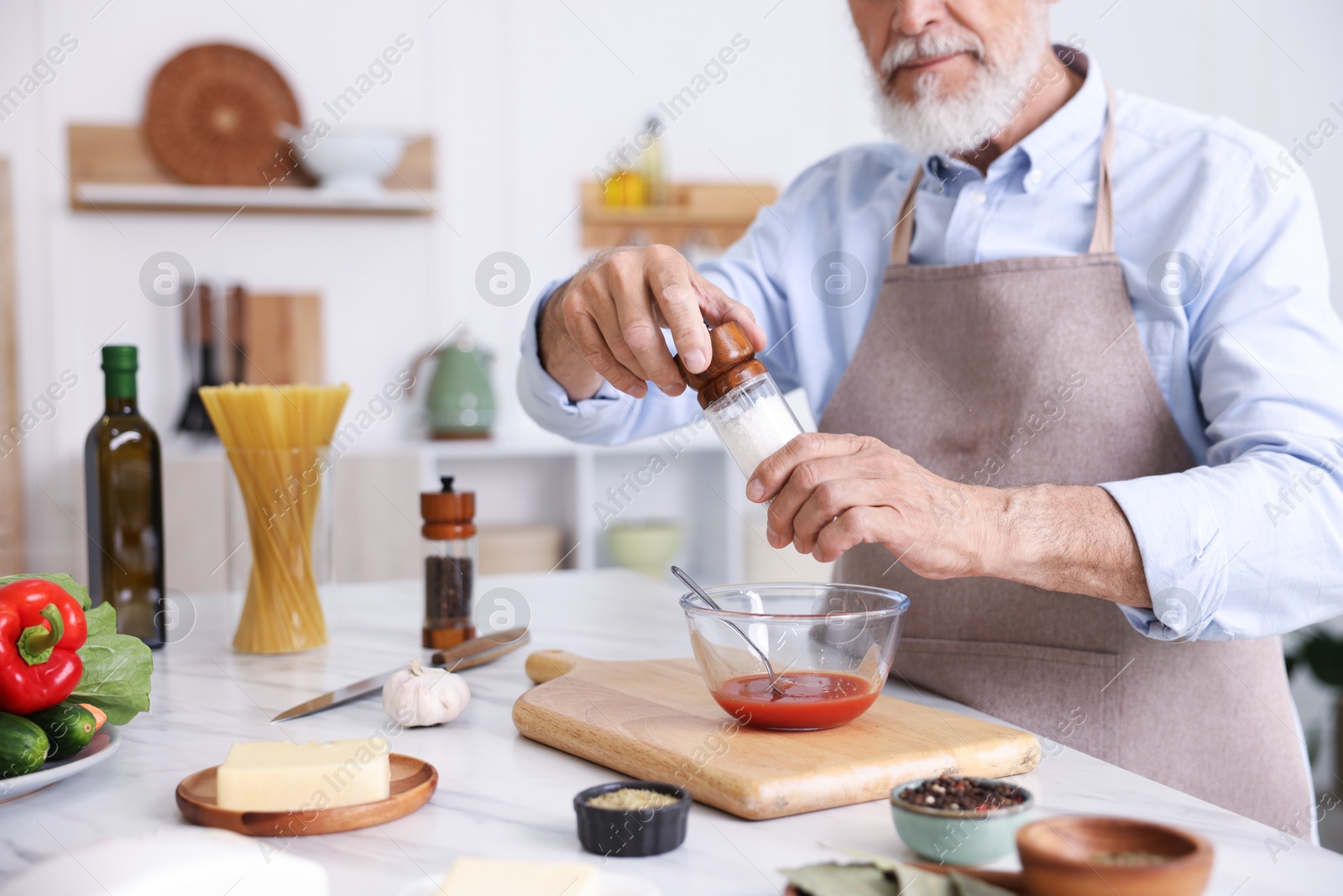 Elderly man cooking at white marble table in kitchen, closeup Photo of Elderly man cooking at white marble table in kitchen, closeup