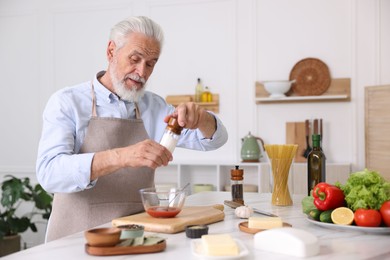Photo of Elderly man cooking at white marble table in kitchen