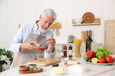 Photo of Elderly man cooking at white marble table in kitchen