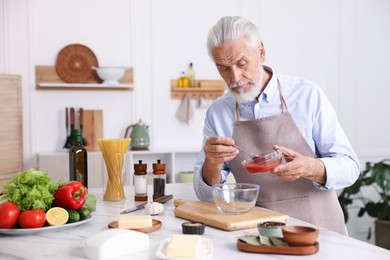 Photo of Elderly man cooking at white marble table in kitchen