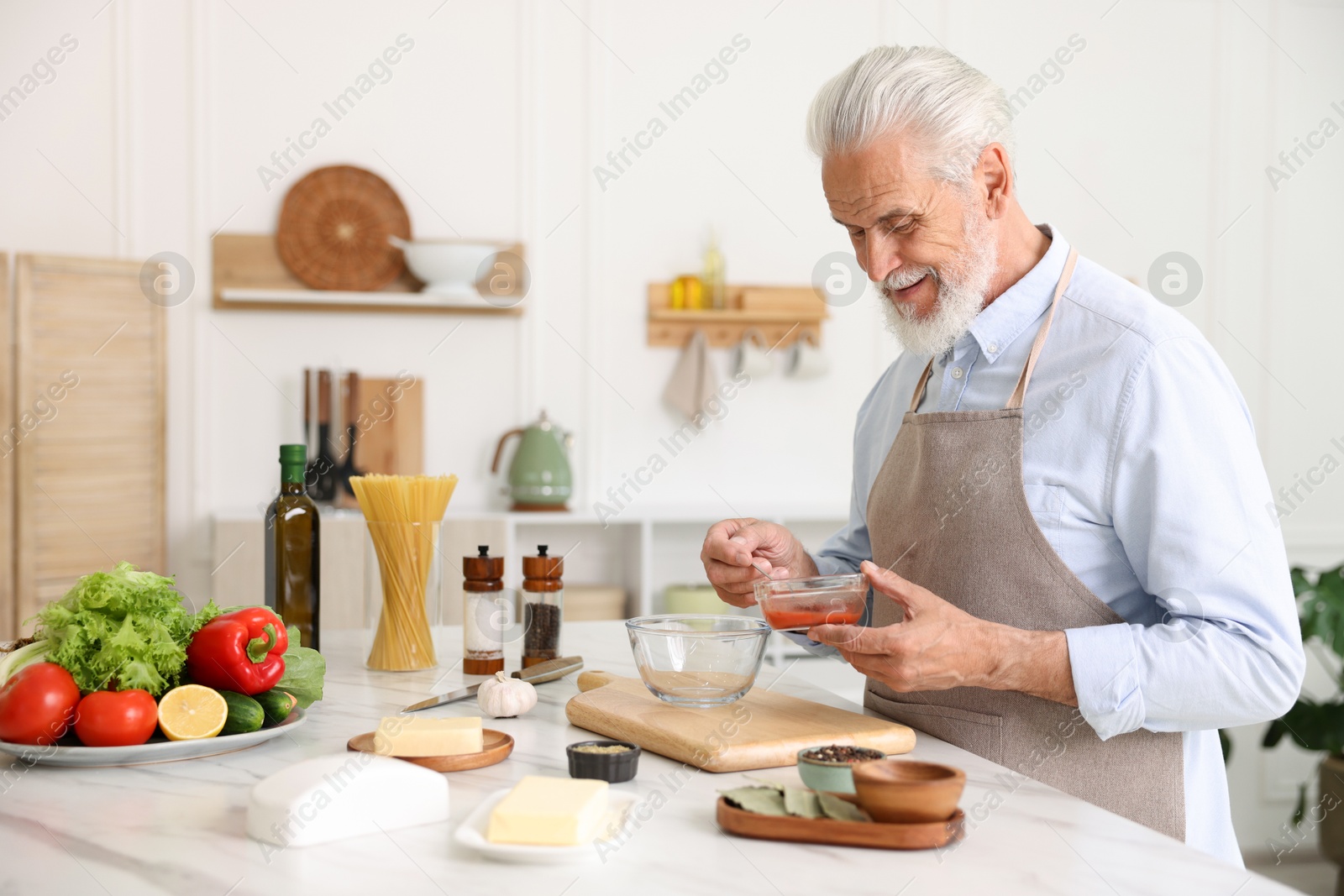 Elderly man cooking at white marble table in kitchen Photo of Elderly man cooking at white marble table in kitchen