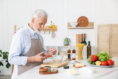 Photo of Elderly man cooking at white marble table in kitchen