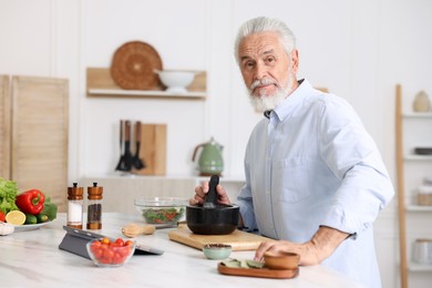 Photo of Elderly man cooking at white marble table in kitchen