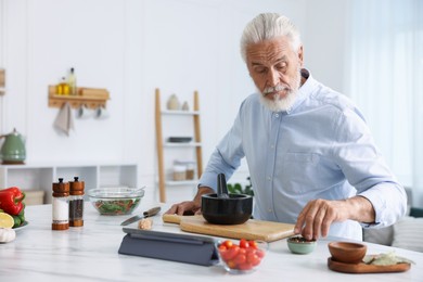 Photo of Elderly man cooking at white marble table in kitchen