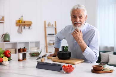 Photo of Elderly man cooking at white marble table in kitchen