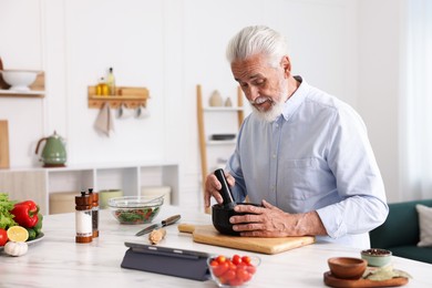 Photo of Elderly man cooking at white marble table in kitchen