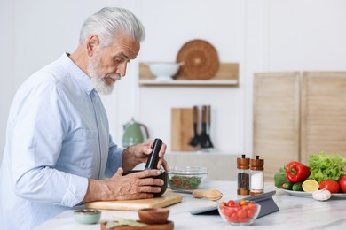 Photo of Elderly man cooking at white marble table in kitchen