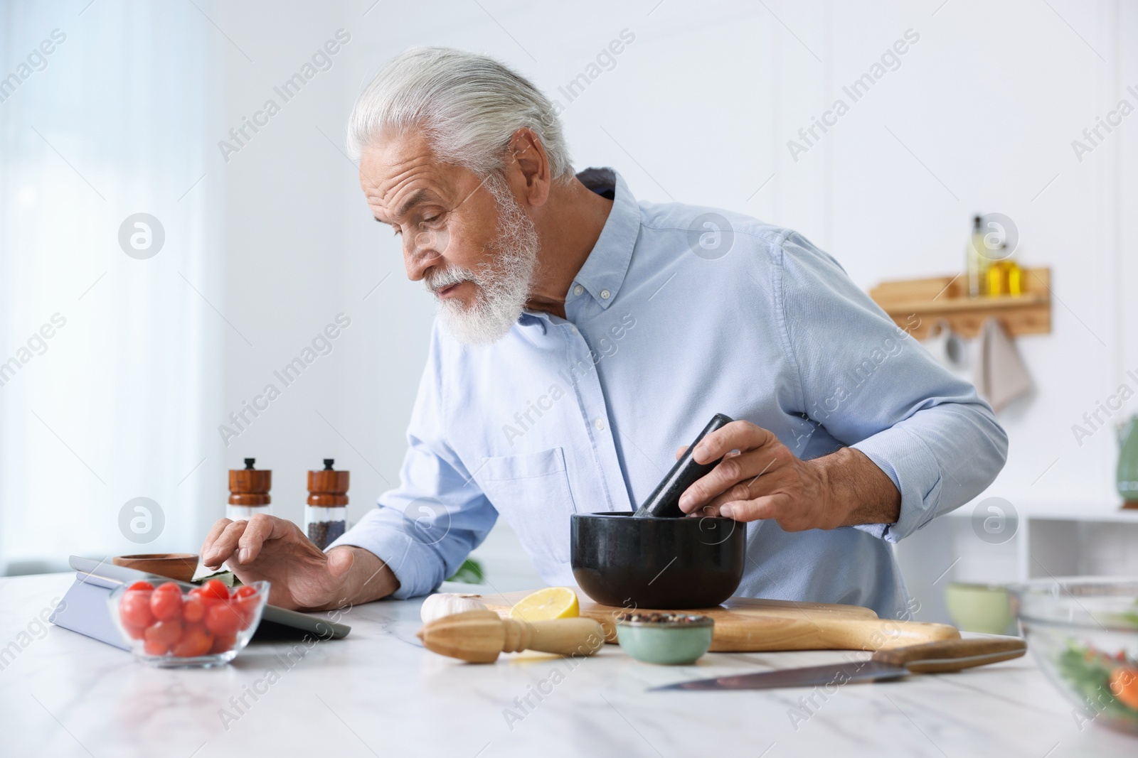 Elderly man using tablet while cooking at white marble table in kitchen Photo of Elderly man using tablet while cooking at white marble table in kitchen